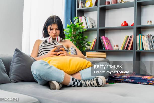 ragazza adolescente che controlla i social media tenendo lo smartphone a casa - topnews foto e immagini stock