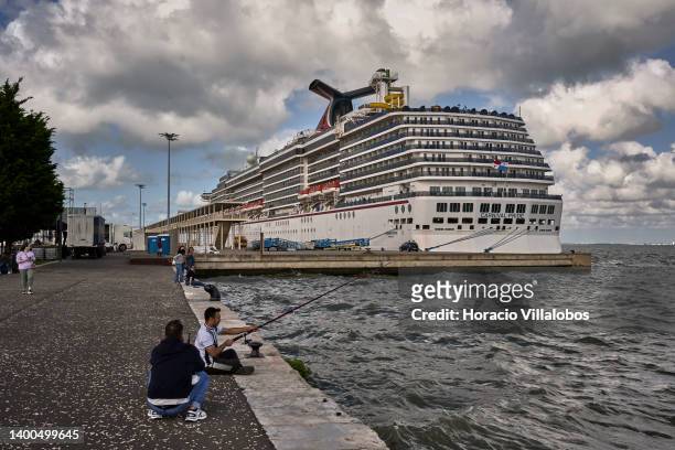 Man is seen fishingn in the Passeio Marítimo da Doca da Marinha while Carnival Pride, a Spirit-class cruise ship operated by Carnival Cruise Line, is...