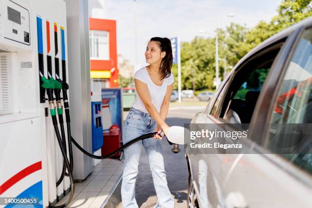 lächelnde frau, die den benzintank an der zapfsäule betankt - refuelling stock-fotos und bilder