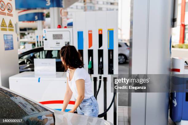 upset woman refueling the gas tank at fuel pump - gasoline pistol stock pictures, royalty-free photos & images