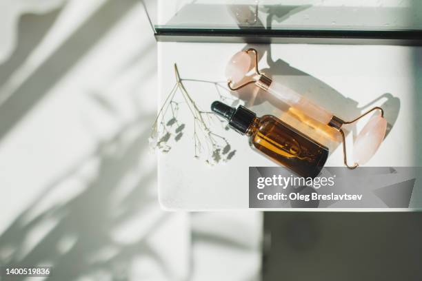 bottle with lotion or essential oil and natural rose quartz face roller massager - mottled skin stockfoto's en -beelden