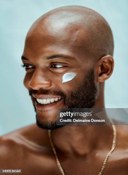 homme afro-américain détournant les yeux et souriant avec une lotion sous les yeux. l’homme chauve est torse nu et porte des bijoux. il a l’air heureux dans le portrait - lounge chair photos et images de collection