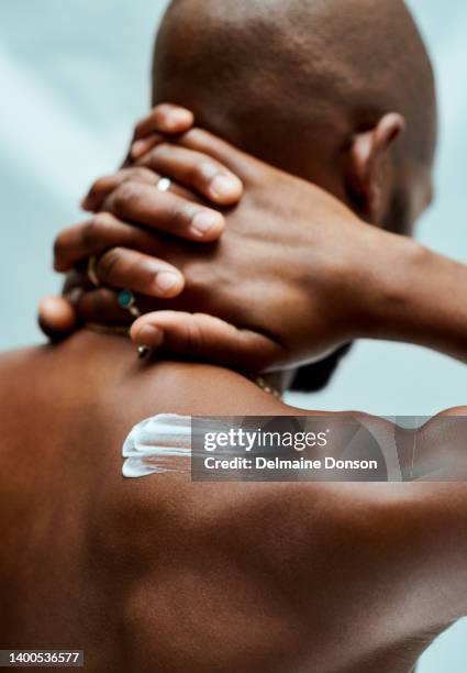 afroamerikaner verschränken seine finger hinter seinem kopf in einem isolierten studiohintergrund. er hat feuchtigkeitscreme auf der schulter und steht alleine - body lotion stock-fotos und bilder