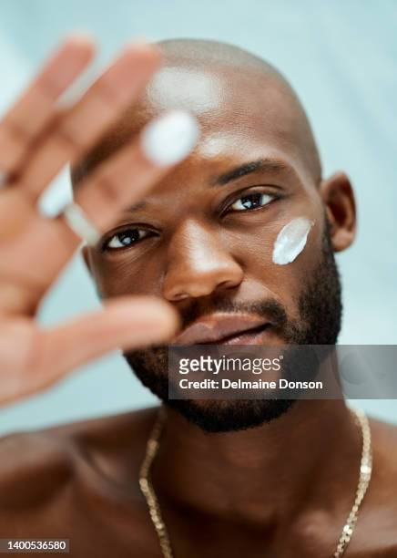 portrait of an african american male model with his hand up. he has lotion in his finger and under his eye.the man is standing alone inside the room - man eye cream stock pictures, royalty-free photos & images