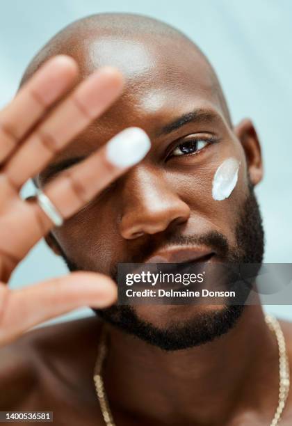 african american male model with his hand up and moisturizer on his cheek. blurry hand and focus on his face. he is doing his skincare routine - man eye cream stock pictures, royalty-free photos & images