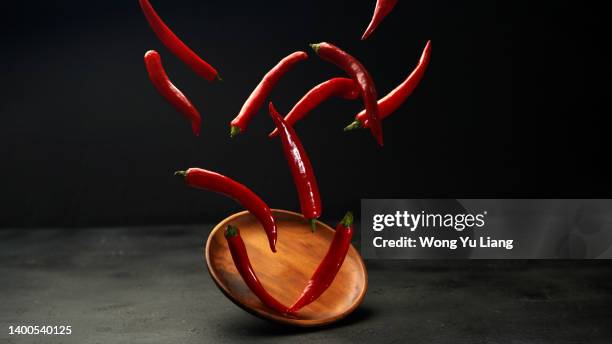 red hot chilli peppers flying freezed motion on dark background - chilli powder stock-fotos und bilder