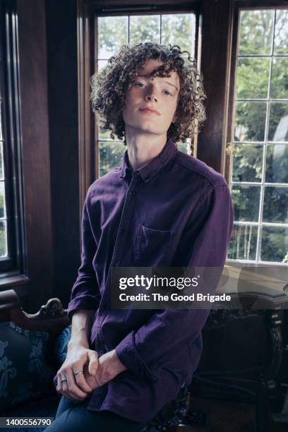 portrait of young man with curly hair standing by window - beautiful gay men stock pictures, royalty-free photos & images