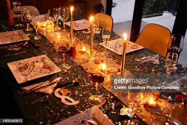 candlelit dining table covered in sparkling confetti during a new year's eve party - party inside stockfoto's en -beelden