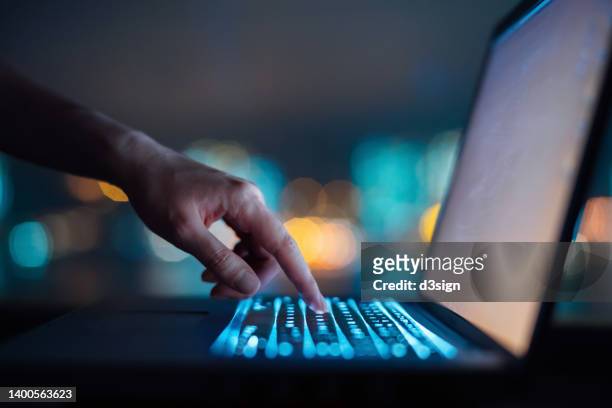 close up of woman's hand typing on computer keyboard in the dark against colourful bokeh in background, working late on laptop at home - access photos et images de collection