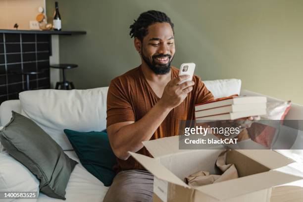 junger mann packt die box aus und macht ein foto von online bestellten artikeln - online shopping opening package stock-fotos und bilder