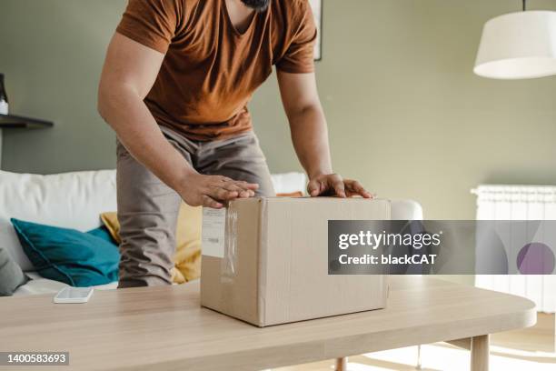 abgeschnittene aufnahme eines jungen mannes beim auspacken des online-kaufs - return stock-fotos und bilder