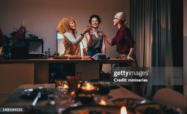 three woman toasting with a glass of wine during a dinner preparation - friends dinner party stockfoto's en -beelden