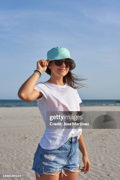 a girl on the beach with a bucket hat and sunglasses enjoying her summer vacation - bucket hat stock pictures, royalty-free photos & images