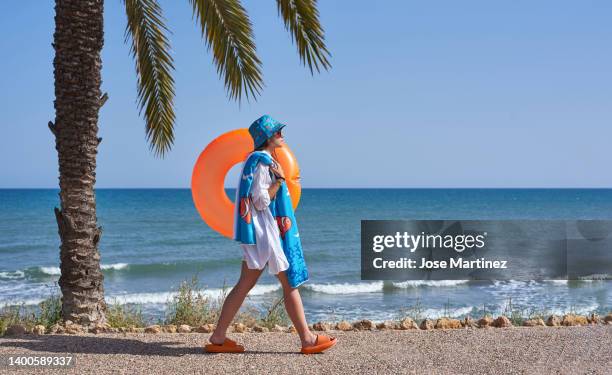 woman walking towards the beach with an orange float and summer clothes - beach sunbathing spain fotografías e imágenes de stock