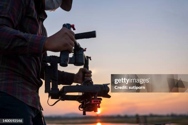 man using a gimbal and stabilizer to shoot a video at sunset - regista cinematografico foto e immagini stock