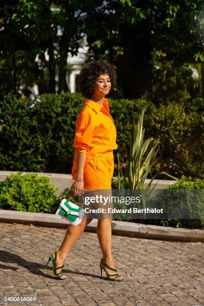 Lena Mahfouf aka Lena Situations wears a full neon orange look, an orange shirt, orange mini shorts, a white and green Bulgari bag, green high heels...