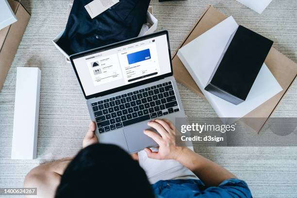 overhead view of asian man shopping online with laptop, making online payment with credit card. with shopping packages and delivery boxes laying out around him at home. online shopping and e-commerce. contactless payment. new shopping habits and routine - banking document stock-fotos und bilder