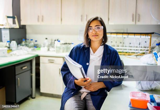 giovane ricercatrice che indossa occhiali protettivi seduta in un laboratorio - biochemical foto e immagini stock