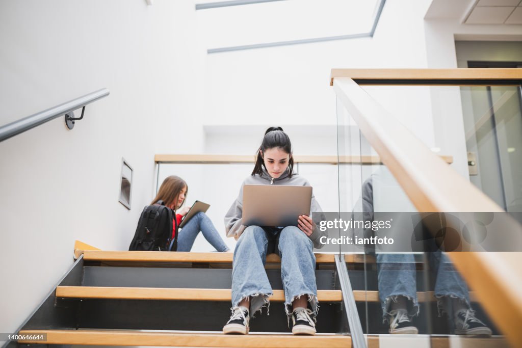 Girl sitting on the high school stairs studing with laptop.