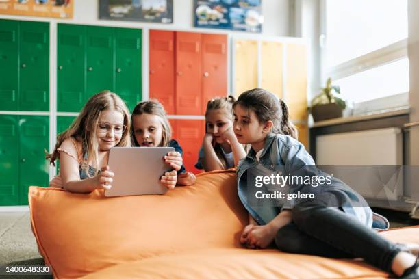 four school girls on bean bag and looking on tablet together - digitization stockfoto's en -beelden