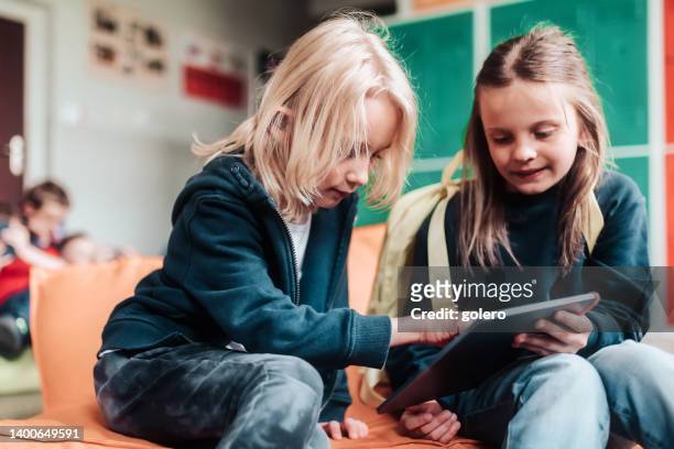elementary school girl and boy on bean bag looking on tablet together - digitalisering bildbanksfoton och bilder