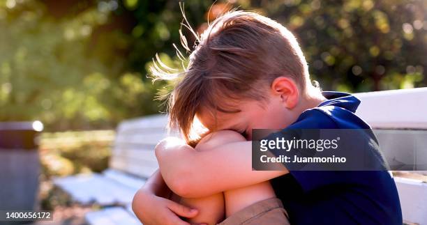 crestfallen crying bambino ragazzo seduto su una panchina che copre il suo viso - scared boy foto e immagini stock