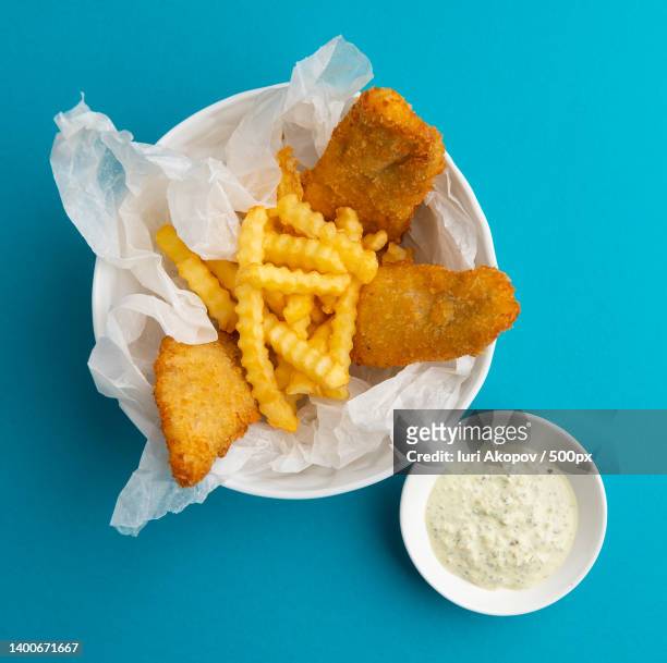 high angle view of breaded fish and french fries in bowl on blue background - fritto foto e immagini stock