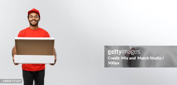 portrait of young delivery man holding cardboard box against white background - delivery person on white stock pictures, royalty-free photos & images