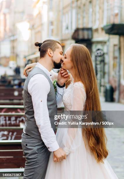 side view of newlywed couple kissing while standing on street - fashion designer married hugging - fotografias e filmes do acervo