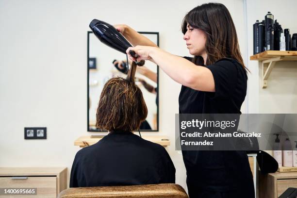 hairdresser combs and dries client's hair. - short hair stock pictures, royalty-free photos & images