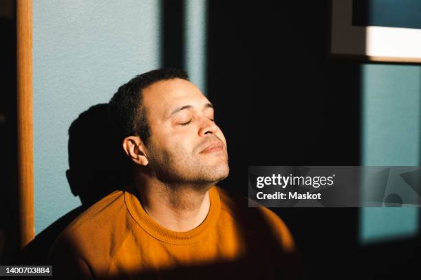 man with eyes closed enjoying sunlight at home - gente serena fotografías e imágenes de stock