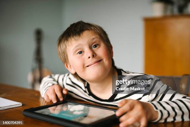 portrait of happy boy with down syndrome sitting at table - down's syndrome stockfoto's en -beelden