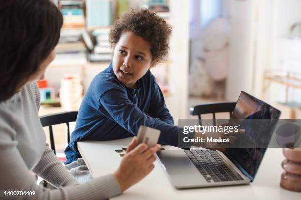 son pointing at laptop screen while looking at mother holding credit card - asking money stock pictures, royalty-free photos & images