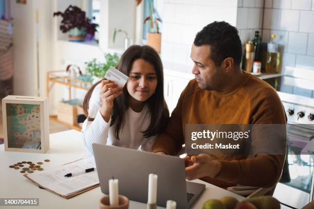father teaching online shopping to daughter on laptop at home - kids money fotografías e imágenes de stock