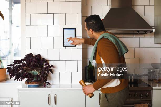 side view of man using home automation device on wall while standing in kitchen at home - smart kitchen stock pictures, royalty-free photos & images