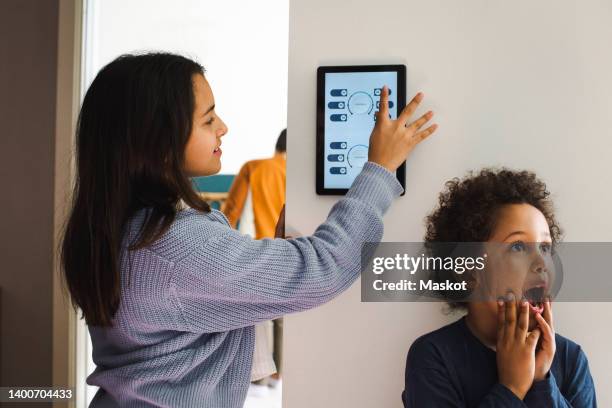 girl using home automation device while standing with surprised brother against wall at home - command sisters photos et images de collection