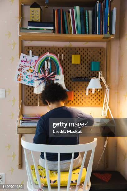 rear view of boy sitting on chair by desk while studying at home - estudiando flexo fotografías e imágenes de stock