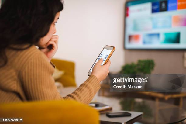 woman controlling tv through smart phone at home - smart tv stock-fotos und bilder