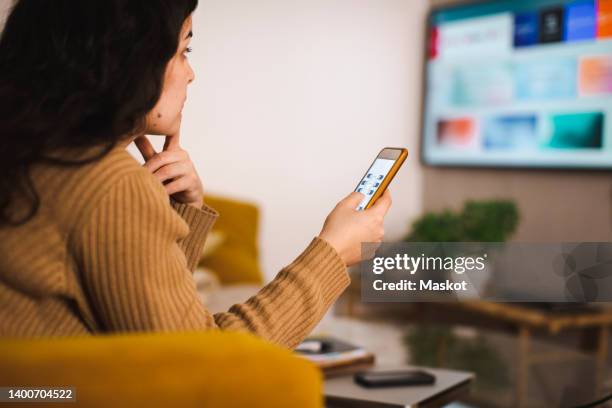 side view of young woman controlling tv through mobile app at home - smart tv fotografías e imágenes de stock