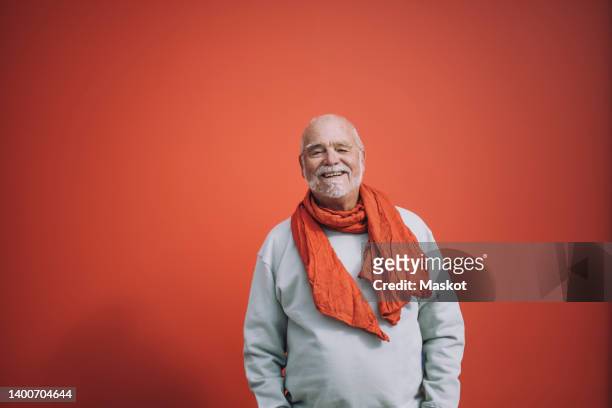portrait of happy senior man standing against orange background - fondo con color fotografías e imágenes de stock