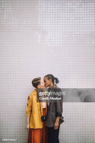 affectionate lesbian couple kissing while standing against wall - kissing stockfoto's en -beelden
