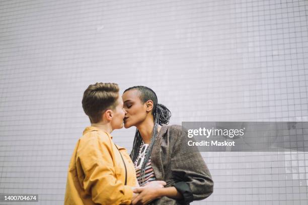 young woman with eyes closed kissing girlfriend while standing against wall - black lesbians kiss stock pictures, royalty-free photos & images