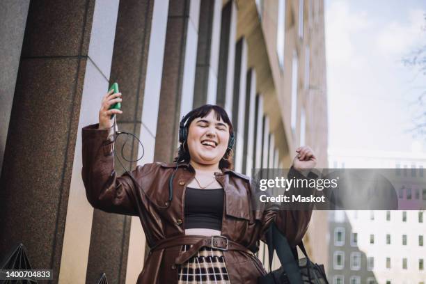happy young woman with eyes closed dancing while listening music through headphones - fat woman dancing stockfoto's en -beelden