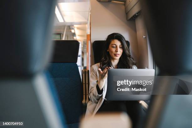 businesswoman talking on video call through laptop while sitting in train - viaggio di lavoro foto e immagini stock