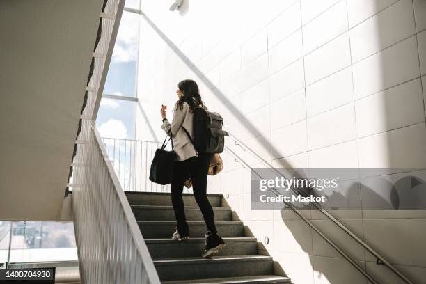 rear view of businesswoman with backpack moving up on staircase at railroad station - walking up stairs stockfoto's en -beelden