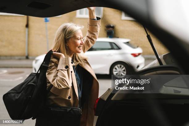 businesswoman carrying luggage while opening car trunk - corporate travel stock pictures, royalty-free photos & images