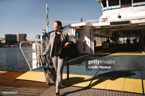 businesswoman pulling wheeled luggage while disembarking from ferry on sunny day - commuter ferry stock pictures, royalty-free photos & images