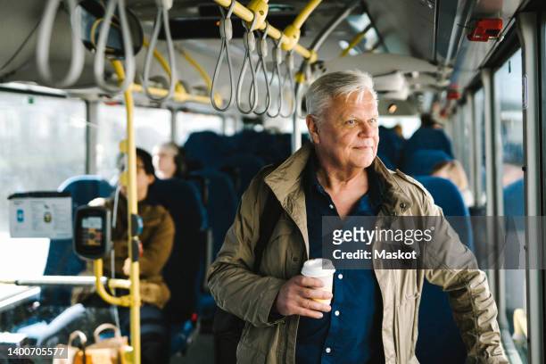 thoughtful businessman holding disposable cup while commuting through bus - people on buses stockfoto's en -beelden