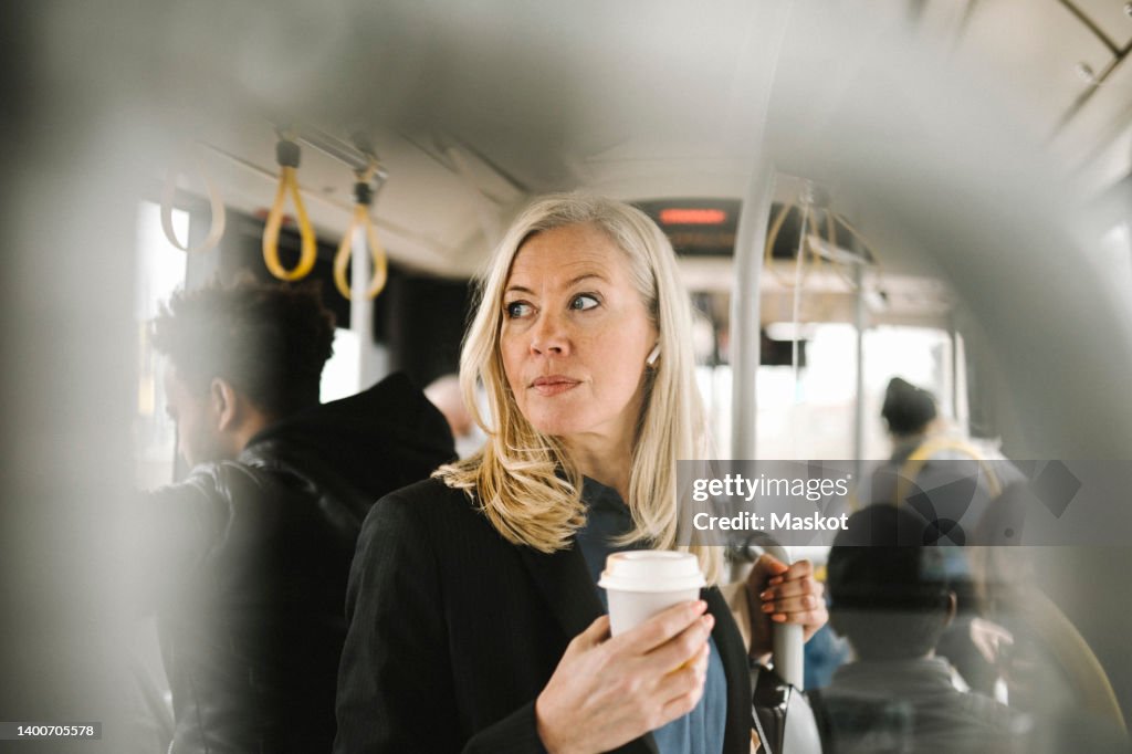 Contemplative businesswoman holding disposable cup while commuting through bus