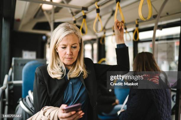 businesswoman holding grab handle while using smart phone in bus - つり革 ストックフォトと画像